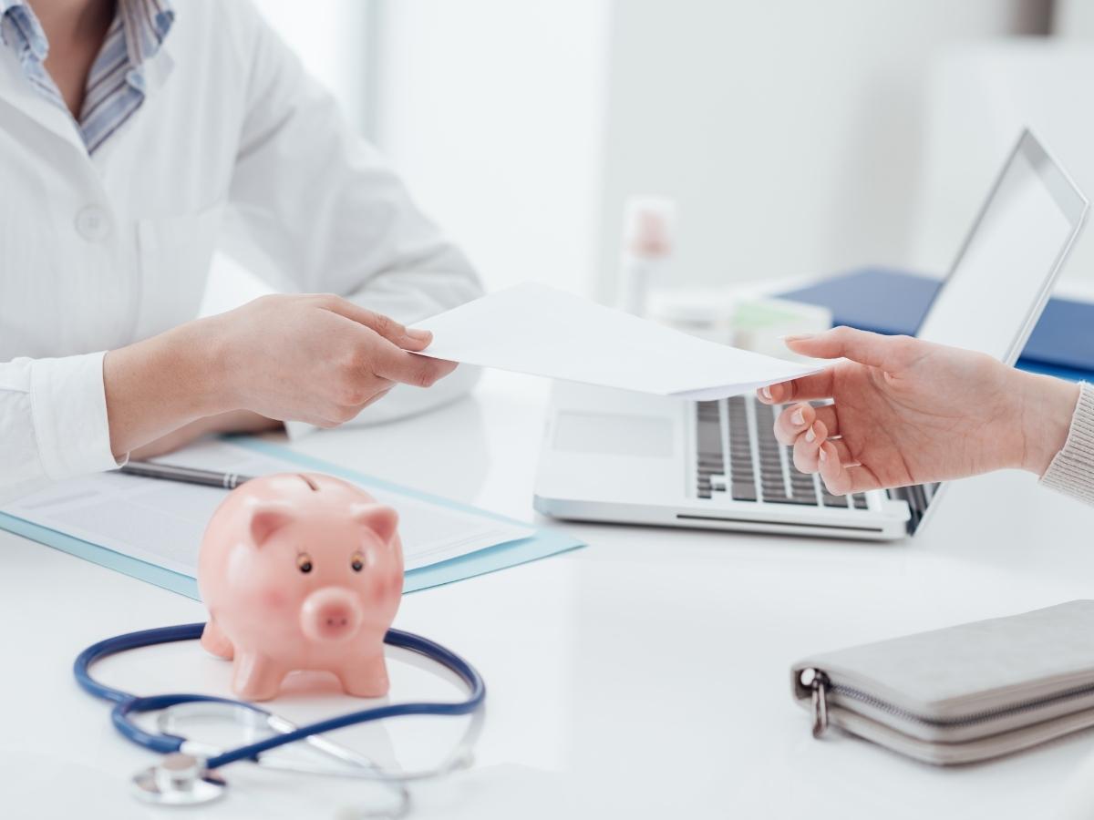 Christian Healthcare Centers offers an expensive healthcare alternative by introducing cost=sharing programs that wont break the piggy bank. A piggy bank sits on a dooctor's office desk while meeting with a patient.