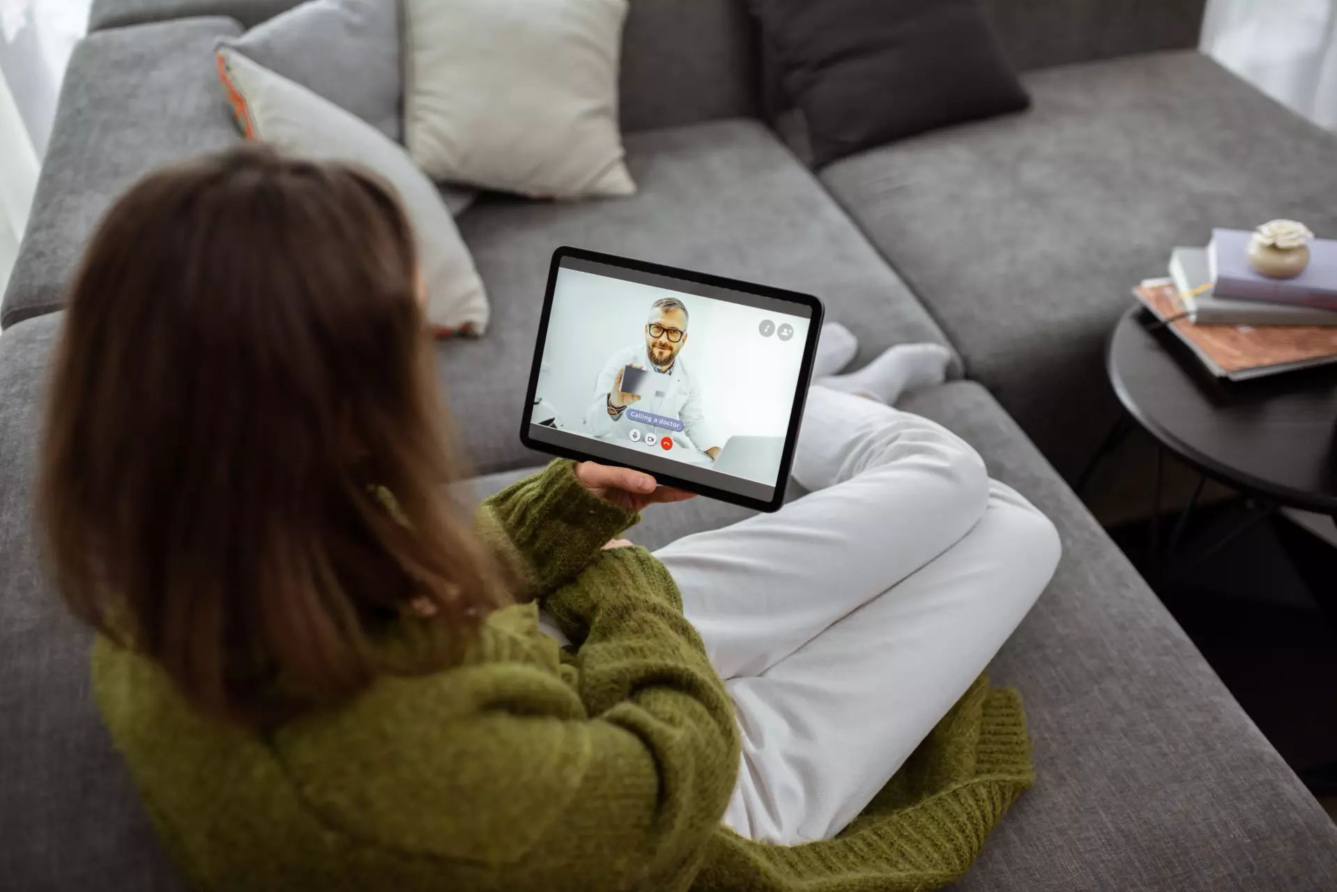 An overhead view of a woman sitting on a couch, talking to a doctor on a tablet. She is using Telehealth for Direct Primary Care.