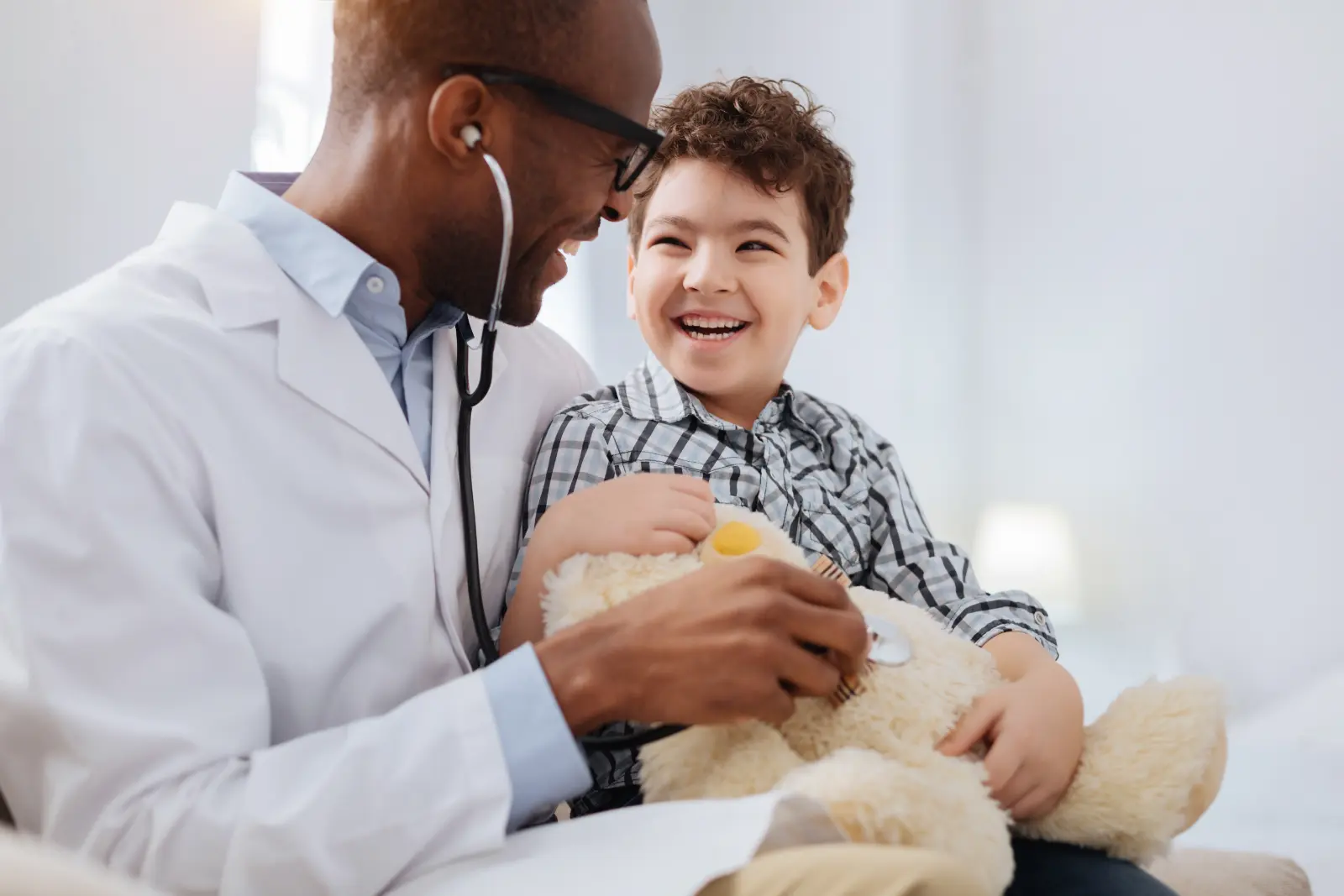 Why Choose Direct Primary. Immediate treatment. Enthusiastic vigorous male doctor sitting with boy while listening to plush bear and talking
