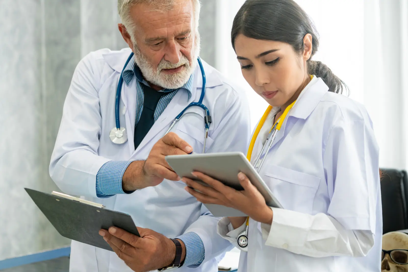 Direct Primary Care. Senior male doctor using tablet computer while discussing with another doctor at the hospital. Medical healthcare staff and doctor service.