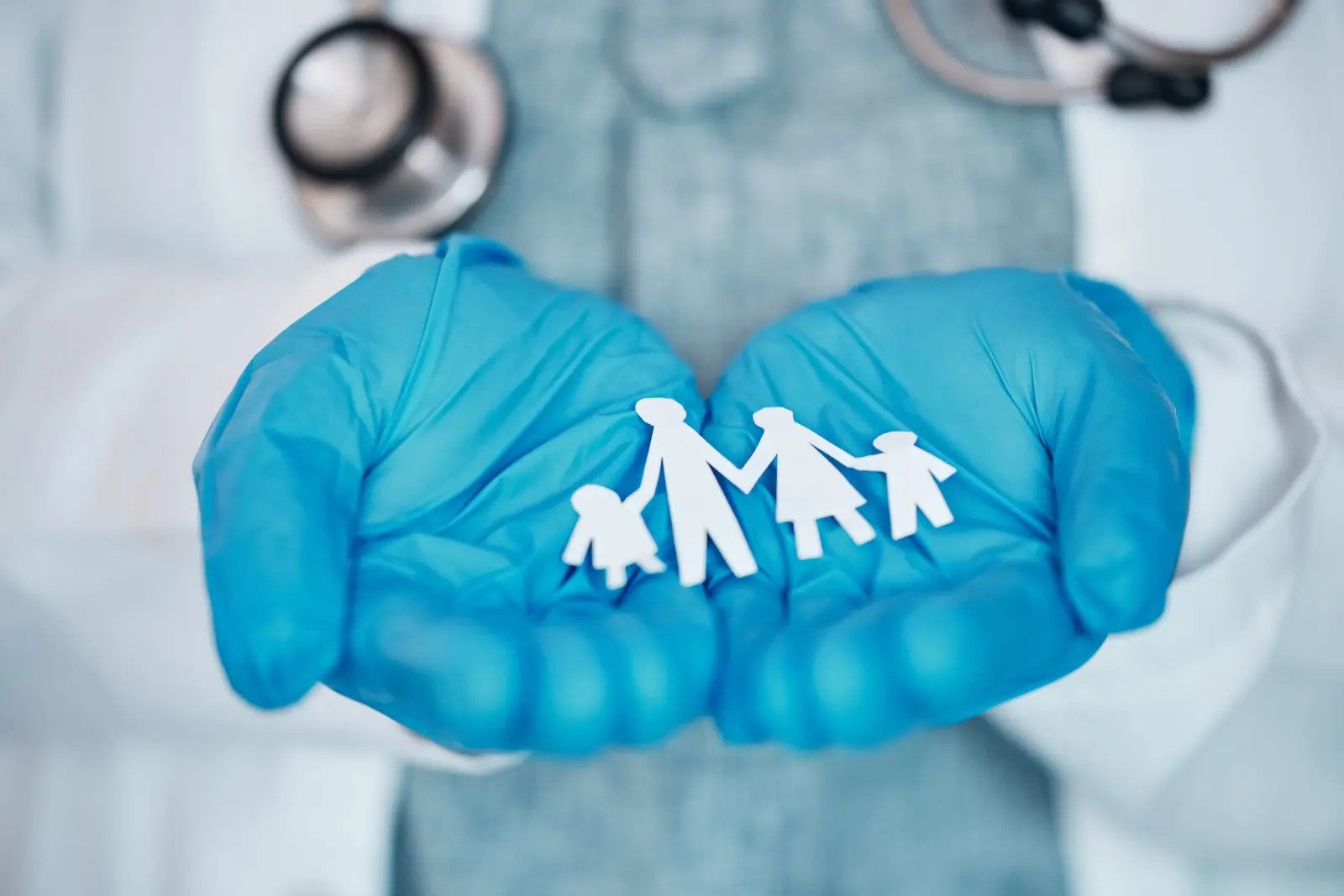 closeup doctors hands holding paper cutout family thinking about the Membership-Based Primary Care